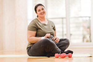 Mid adult fat woman resting after exercising. She is sitting on the floor and looking at the camera.